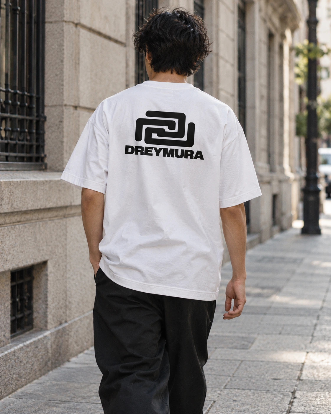 Man wearing the white Dream Village T-shirt with a large black DREYMURA back print
