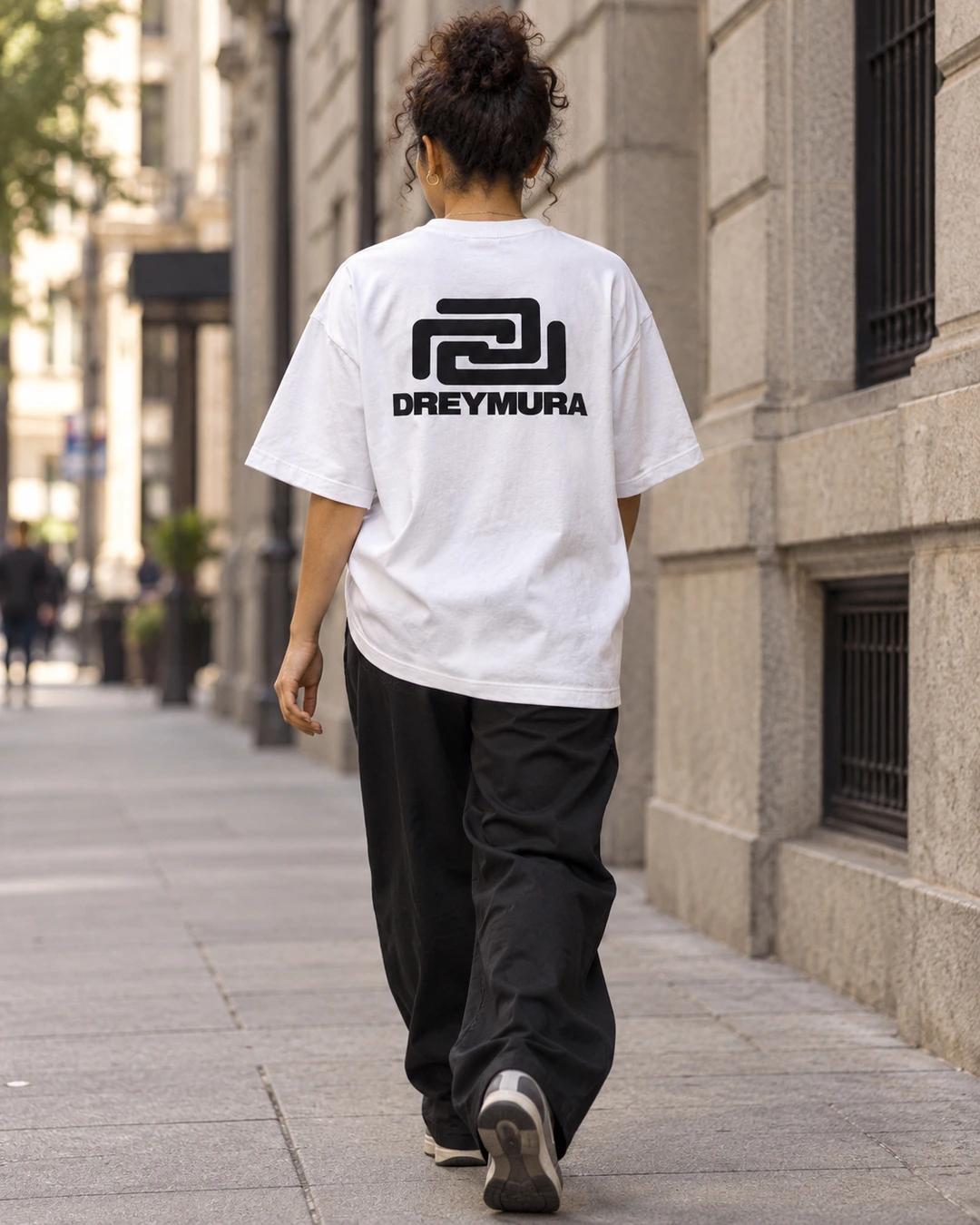 Woman wearing the white Dream Village T-shirt with the DREYMURA symbol and wordmark on the back